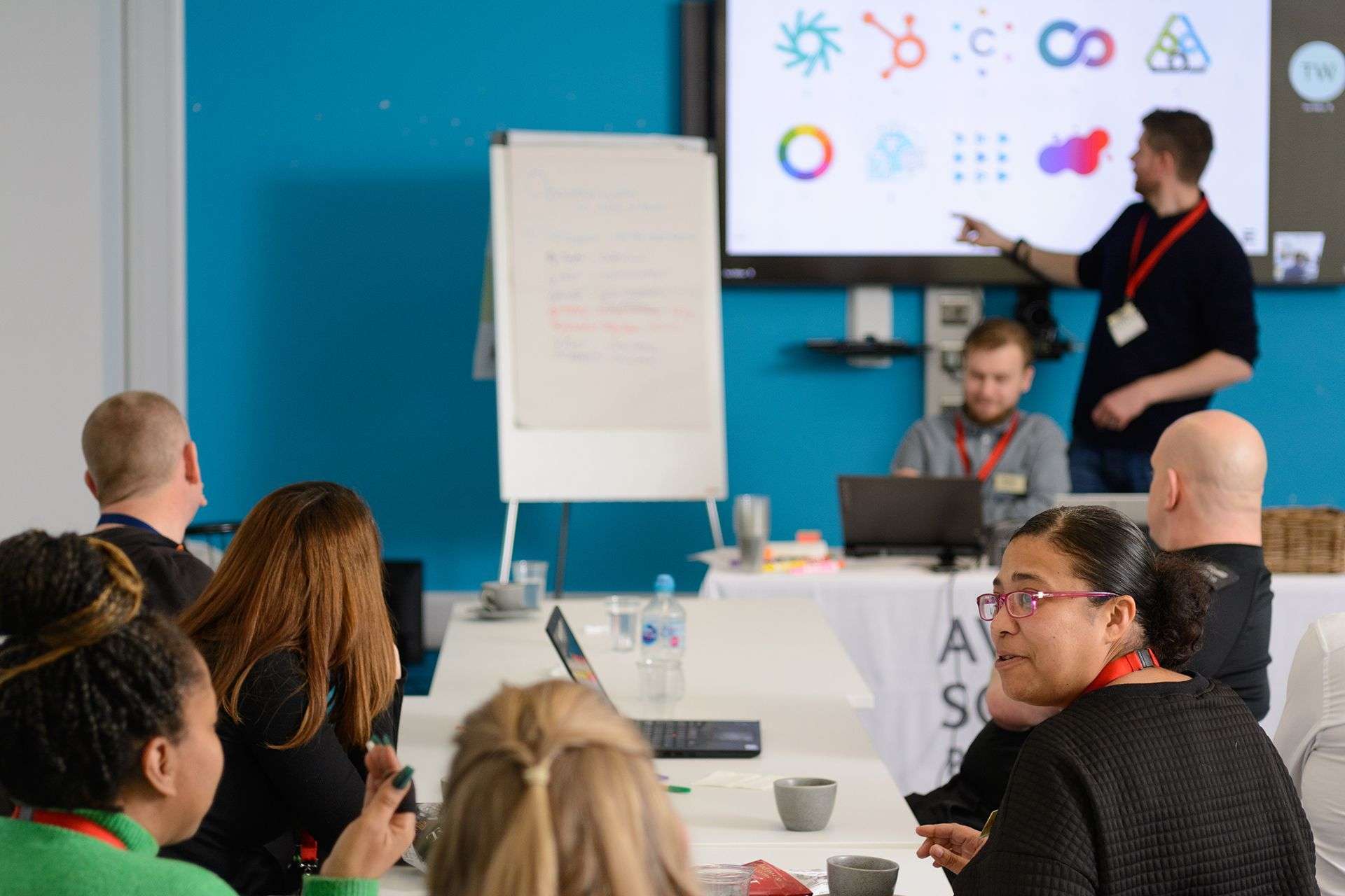 Our creative director Tom Walton pointing at a screen of company logos in front of an audience during a workshop